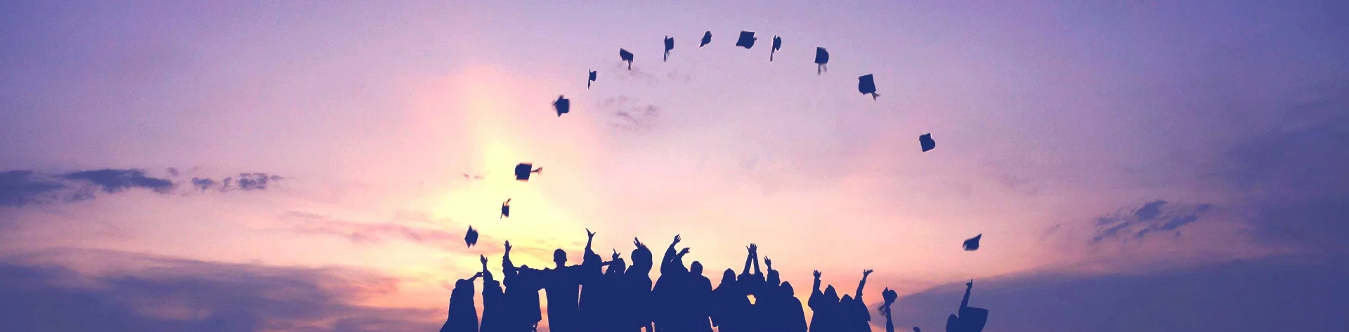 Students toss up their graduation hats at sunset.